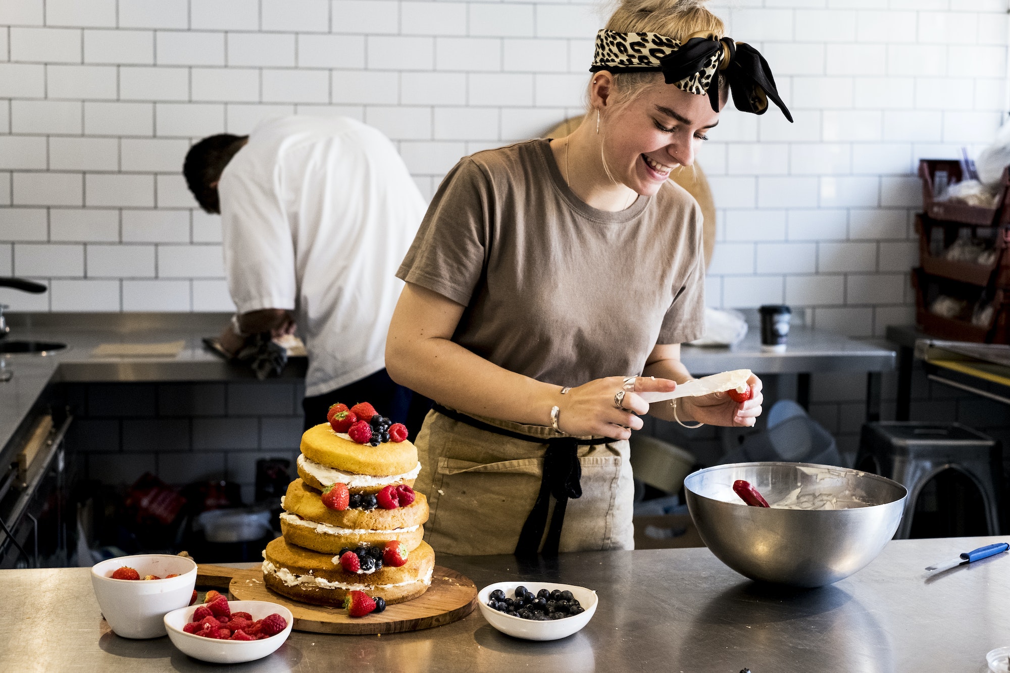 a-cook-working-in-a-commercial-kitchen-assembling-a-layered-sponge-cake-with-fresh-fruit-.jpg